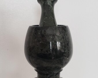 May include: A black and green marble mortar and pestle. The mortar has a wide base and a rounded bowl. The pestle is smooth and has a rounded top.