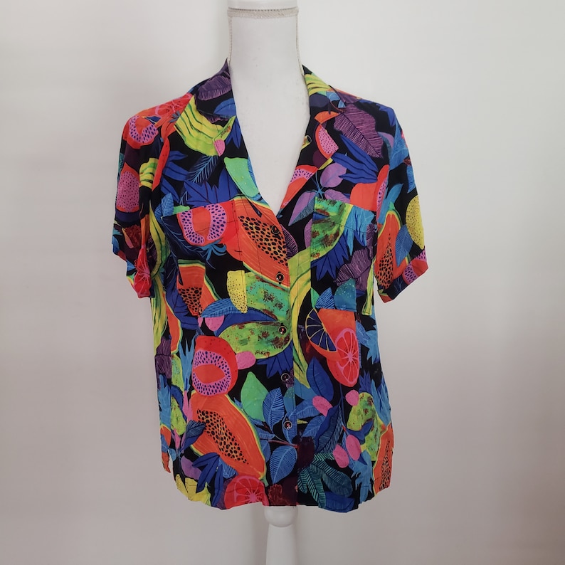 May include: A short-sleeved button-up shirt with a colorful tropical fruit print. The shirt is made of a lightweight fabric and has a relaxed fit.