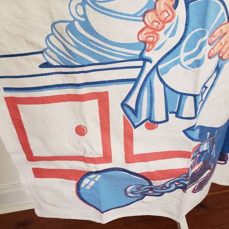 May include: A white kitchen towel with a blue and red illustration of a person holding a dish towel and a blue ball and chain. The illustration is on a white background with red and blue squares.