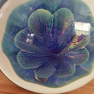 Könnte beinhalten: Ein Glas-Briefbeschwerer mit einem blauen und grünen, schillernden Blumendesign.