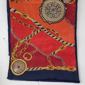 May include: A red and navy blue silk scarf with a gold chain and pocket watch design. The watch face has Roman numerals and a gold trim.