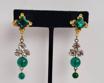 May include: A pair of dangle earrings with a green square stone at the top, followed by three clear round stones and two green round stones.