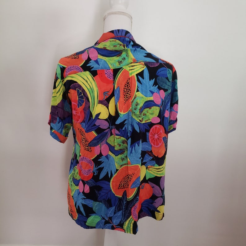 May include: A short-sleeved button-up shirt with a colorful tropical fruit print. The shirt is black with bright orange, yellow, green, and pink fruits.