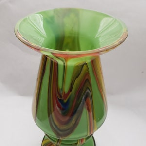 May include: A green glass vase with a wide mouth and a swirling pattern of red, orange, yellow, blue, and black.