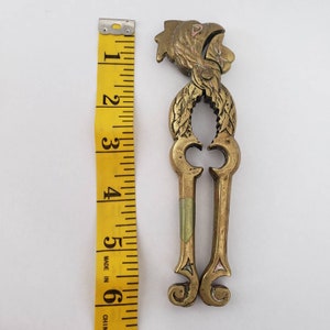 May include: Brass nutcracker with a rooster design. The rooster is painted with pink, green, and yellow accents. The nutcracker is about 6 inches tall.