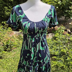 Puede incluir: Vestido con estampado floral azul marino y verde, con escote en forma de U y mangas cortas. El vestido tiene un corpi&ntilde;o ajustado y una falda escalonada. El vestido se exhibe en un maniqu&iacute; blanco en un entorno al aire libre.