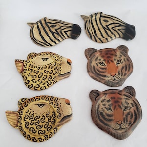 May include: Six different coasters featuring animal prints. The coasters are made of wood and have a painted finish. The animals featured are a zebra, a leopard, and a tiger.