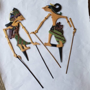 May include: Two traditional Indonesian shadow puppets, one male and one female, with painted details and intricate designs. The puppets are made of wood and have movable limbs controlled by sticks.