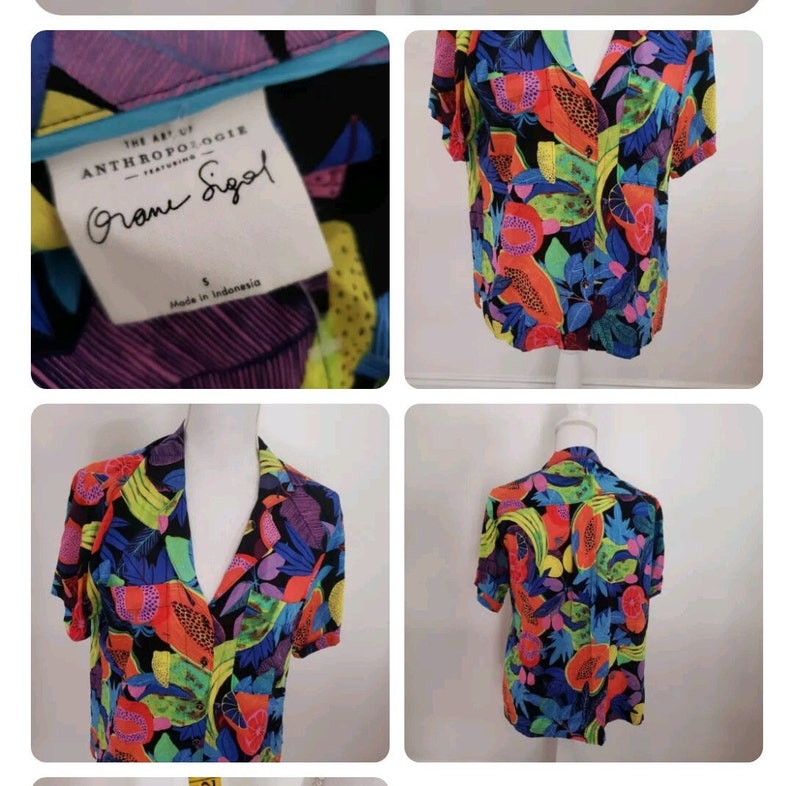 May include: A black short-sleeved button-up shirt with a colorful tropical fruit print. The shirt has a collar and a button-up front. The print features papaya, bananas, and other tropical fruits in shades of red, orange, yellow, green, blue, and purple. The shirt is made by Anthropologie and features the text "The Art of Anthropologie featuring  " in a white font. The shirt is size small and made in Indonesia.