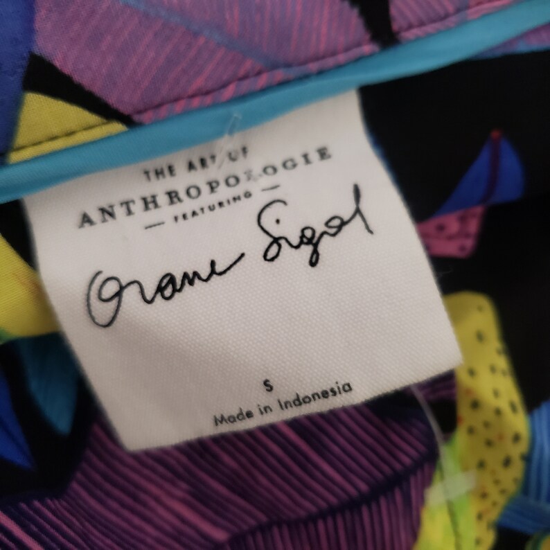May include: White tag with black text that reads "The Art of Anthropologie - Featuring -" followed by a handwritten signature that reads "Diane Sigal". Below the signature is the size "S" and the text "Made in Indonesia".