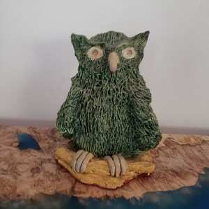May include: A green ceramic owl figurine with white eyes and a beak, perched on a yellow and brown base.
