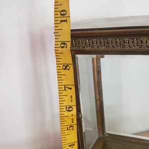 K&ouml;nnte beinhalten: Eine kleine, rechteckige Vitrine aus Glas mit einem Messingrahmen. Die Vitrine hat einen dekorativen Rand oben und unten. Die Vitrine ist etwa 23 cm hoch.