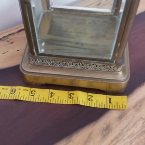 K&ouml;nnte beinhalten: Eine Vitrine aus Messing mit einer Glasplatte und einem dekorativen Rand. Die Vitrine steht auf einer Holzoberfl&auml;che mit einem gelben Ma&szlig;band.