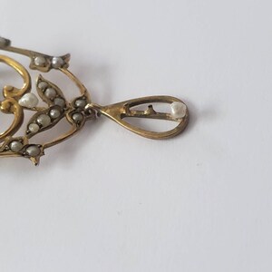 May include: A gold pendant with a teardrop shape and a pearl at the bottom. The pendant is decorated with a delicate floral design and small pearls.