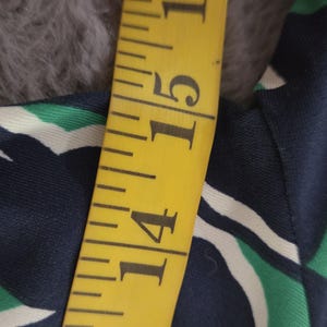 Puede incluir: Una cinta m&eacute;trica amarilla muestra una medida de 35.5 cm. La cinta est&aacute; junto a una tela con un estampado geom&eacute;trico azul marino, blanco y verde. La tela est&aacute; sobre una superficie gris y difusa.