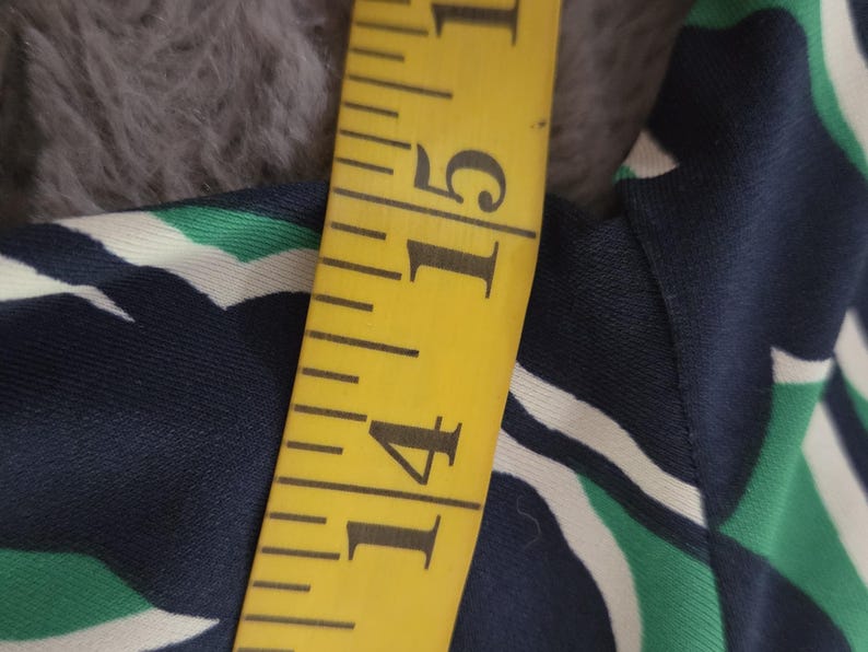 Puede incluir: Una cinta m&eacute;trica amarilla muestra una medida de 35.5 cm. La cinta est&aacute; junto a una tela con un estampado geom&eacute;trico azul marino, blanco y verde. La tela est&aacute; sobre una superficie gris y difusa.