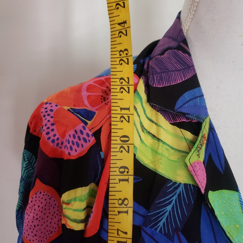 May include: A black button-up shirt with a colorful tropical fruit print. The shirt features bananas, pineapples, and other fruits in shades of red, yellow, green, blue, and pink.