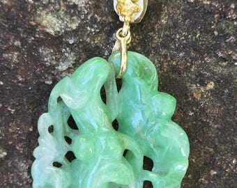 May include: A light green carved jade pendant featuring an intricate openwork design of intertwined mythical creatures. The pendant is suspended from a gold-toned metal bail that is accented with a small, textured gold-colored decorative element.