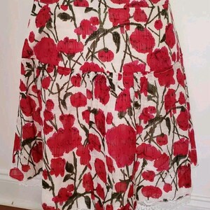May include: A white skirt with a red floral pattern. The skirt features a ruffled hem and a white lace trim along the bottom edge. The floral design includes red flowers and green leaves.