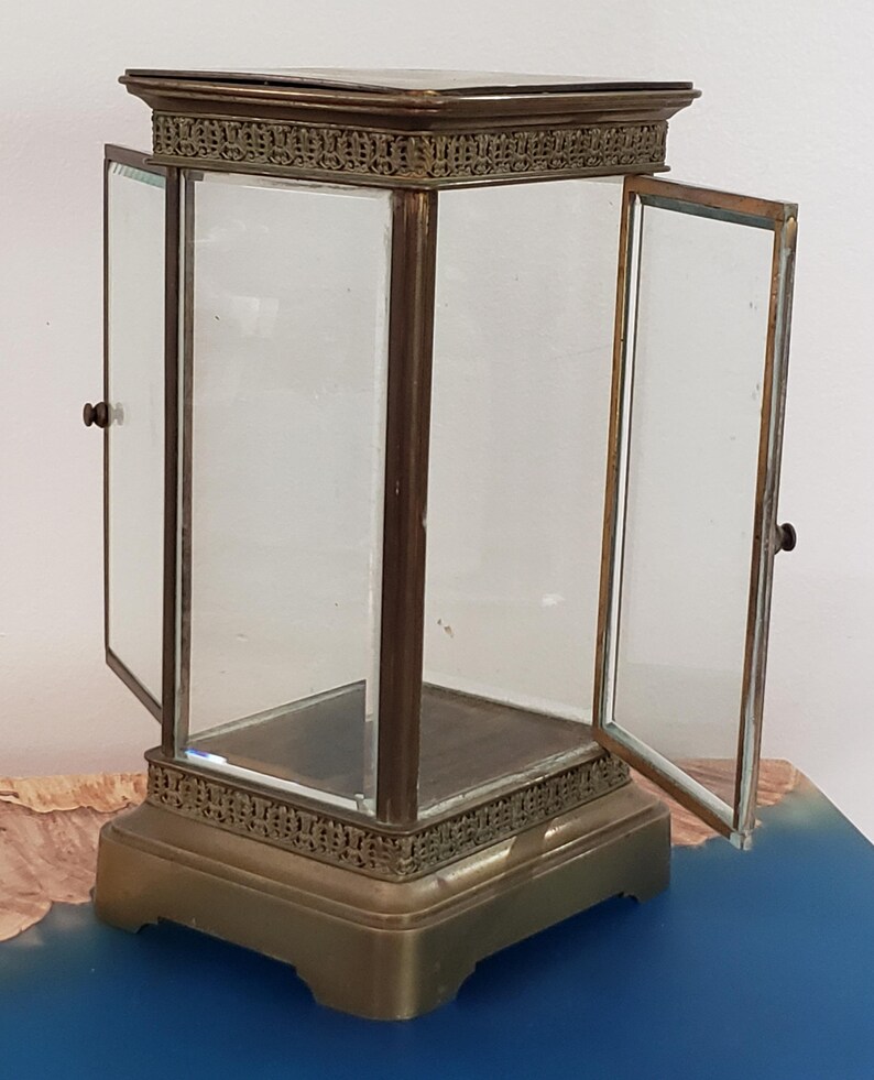 K&ouml;nnte beinhalten: Eine Vitrine aus Messing mit Glast&uuml;ren und einem Glasboden. Die Vitrine hat einen dekorativen Rand um die Ober- und Unterseite. Die T&uuml;ren sind offen und die Vitrine ist leer.