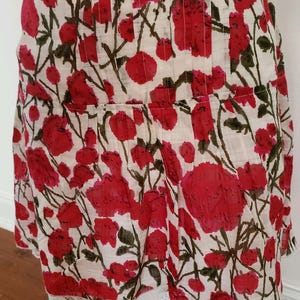 May include: A white and red floral print dress with a pleated bodice and a lace hem. The dress features a pattern of large red flowers with green stems and leaves against a white background. The fabric appears lightweight.