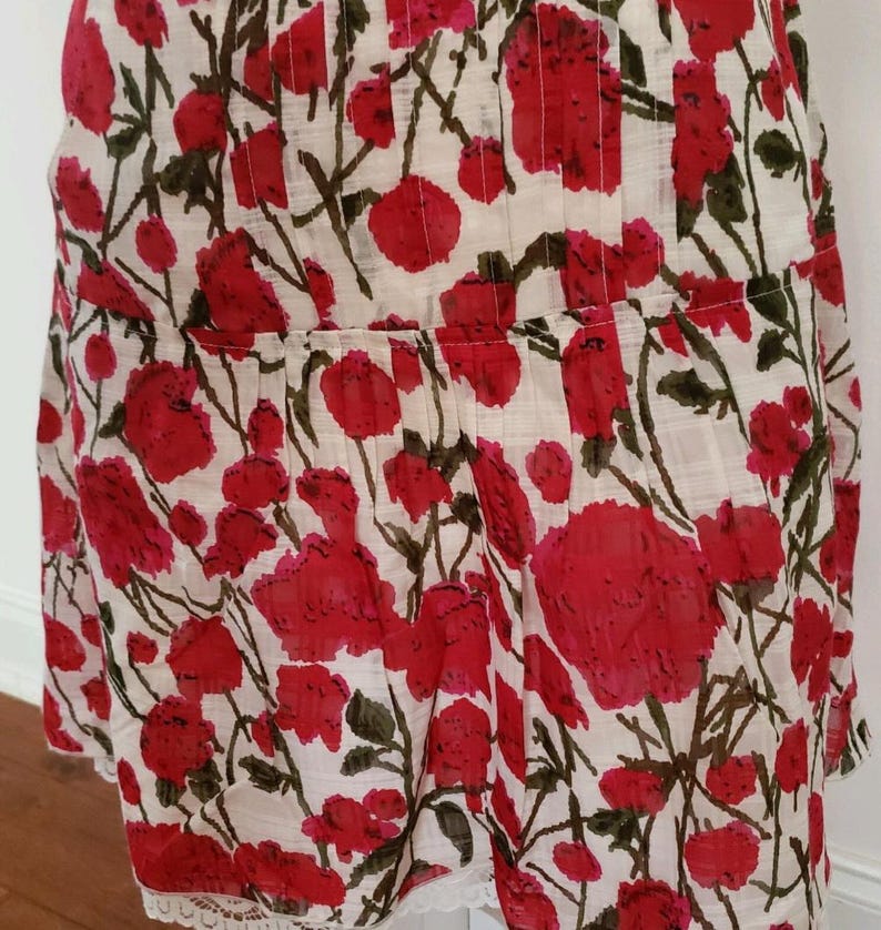 May include: A white and red floral print dress with a pleated bodice and a lace hem. The dress features a pattern of large red flowers with green stems and leaves against a white background. The fabric appears lightweight.
