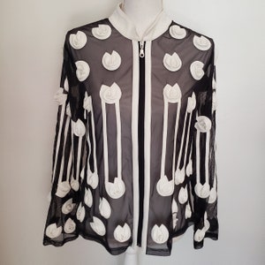 May include: Black mesh jacket with white floral accents and vertical stripes. The jacket features a white collar, a full-length zipper, and decorative white flower appliques. A unique fashion statement.