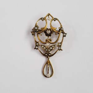 May include: A gold pendant brooch with a teardrop design. The pendant is adorned with small pearls and a single diamond in the center.