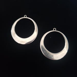 May include: Two silver hoop earrings with a smooth, rounded, crescent moon shape.