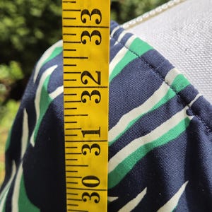 Puede incluir: Primer plano de una tela estampada en azul marino, verde y blanco. Una cinta m&eacute;trica amarilla muestra una longitud de 74 a 84 cm. La tela es probablemente parte de una prenda, posiblemente un vestido o una blusa.