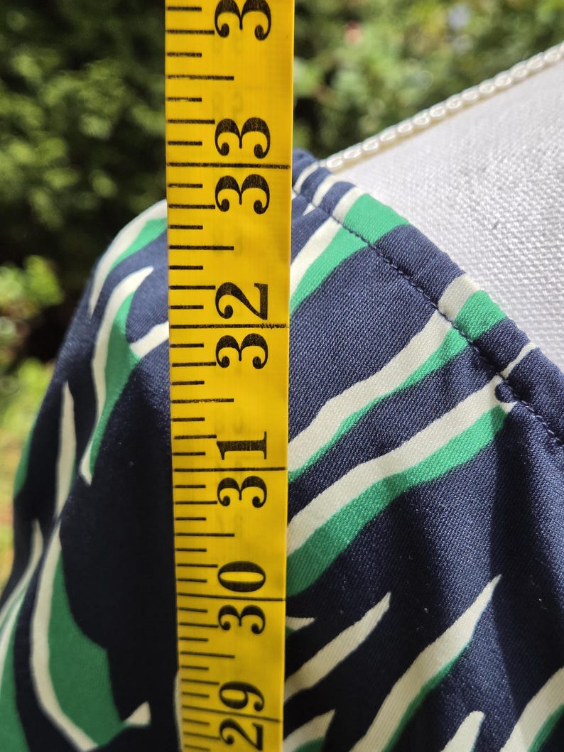 Puede incluir: Primer plano de una tela estampada en azul marino, verde y blanco. Una cinta m&eacute;trica amarilla muestra una longitud de 74 a 84 cm. La tela es probablemente parte de una prenda, posiblemente un vestido o una blusa.