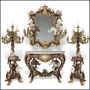 May include: A luxurious antique furniture set featuring a mirror, a console table, and two candelabras. The pieces are intricately carved with ornate details, including figures riding rhinoceroses and elephants, and are finished in a rich brown and gold color scheme.