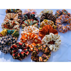 May include: A collection of colorful fabric scrunchies with fall-themed prints, including pumpkins, leaves, and plaid patterns.