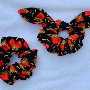 May include: Two black scrunchies with a red and yellow french fry pattern. One scrunchie is tied in a bow.