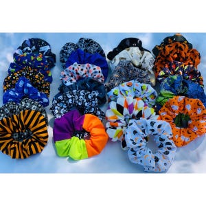May include: A collection of 18 Halloween-themed scrunchies in various colors and patterns, including black, orange, white, purple, and green. The scrunchies feature designs such as ghosts, pumpkins, spiders, and bats.