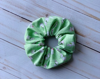 May include: A light green scrunchie featuring a pattern of white bunnies with pink details. The fabric has a textured look. This hair accessory is ideal for adding a playful touch to any hairstyle.