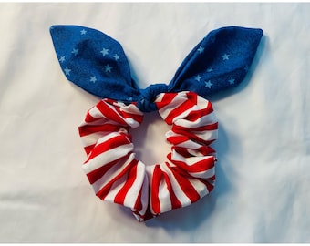 Puede incluir: Una scrunchie patriótica con lazo, con rayas rojas y blancas y una sección azul con estrellas blancas. Este accesorio para el cabello es perfecto para añadir un toque de Americana a cualquier peinado.
