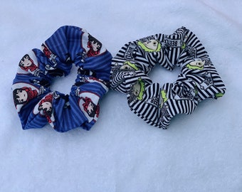 May include: Two fabric scrunchies, one blue with a white stripe and a cartoon character design, and one black and white striped with a cartoon character design.
