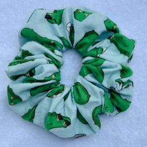 May include: A light blue scrunchie with a repeating pattern of green cartoon pickles wearing sunglasses.