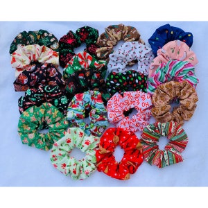 May include: A collection of 20 Christmas-themed scrunchies in various colors and patterns, including red, green, white, brown, and blue. The scrunchies feature holiday designs such as candy canes, reindeer, snowflakes, and the words "Ho Ho Ho".