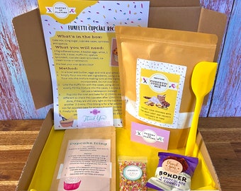 Puede incluir: Una caja amarilla con un kit de horneado de cupcakes funfetti. El kit incluye una bolsa de mezcla para pastel, una bolsa de chispas, una espátula, una bolsa de chispas de chocolate y una tarjeta de receta. La caja está etiquetada "Funfetti Cupcake Recipe".