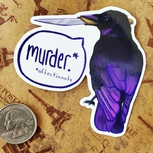 May include: A sticker of a purple and black crow holding a knife in its beak. The crow is looking to the right. The sticker has a speech bubble that says "murder.* *affectionate."