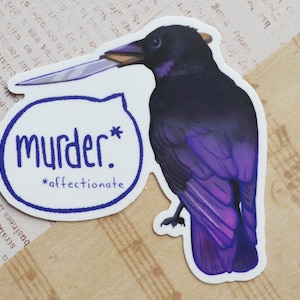 May include: A sticker featuring a purple and black crow holding a silver knife in its beak. The crow is perched on a white background with a blue circle that says "murder*" and "*affectionate" in blue text.
