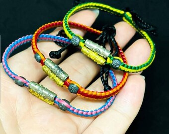 May include: Four colorful braided bracelets with silver charms. The bracelets are layered on top of each other and feature a variety of colors, including pink, blue, red, and green.