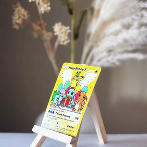 May include: A yellow "Happy Birthday V" card featuring cartoon characters, balloons, and the text "Birthday Celebration." The card is displayed on a small wooden easel. The text "Present Opening" is visible on the card.