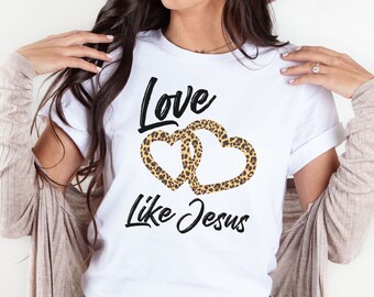 May include: White t-shirt with a black graphic that says "Love Like Jesus" with two intertwined leopard print hearts.