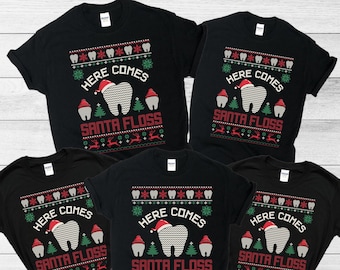 May include: Five black short-sleeve t-shirts featuring a holiday-themed graphic with a central tooth wearing a Santa hat. The design includes the text "HERE COMES SANTA FLOSS" surrounded by patterns of teeth, snowflakes, pine trees, and reindeer.