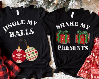 May include: Two black t-shirts with Christmas-themed graphics. One shirt says "JINGLE MY BALLS" with ornament illustrations. The other says "SHAKE MY PRESENTS" with gift box illustrations. Festive holiday apparel.
