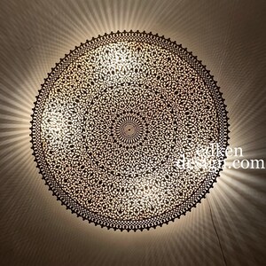 May include: A round, intricate, metal ceiling light fixture with a geometric pattern. The light is on and casting a warm glow.