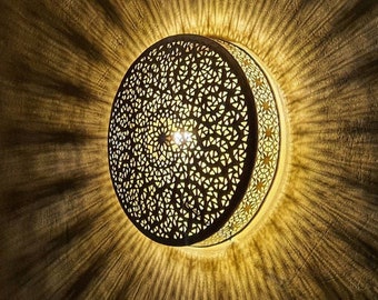 May include: A round, decorative ceiling light fixture with a intricate, geometric pattern. The light is on and casting a warm glow.